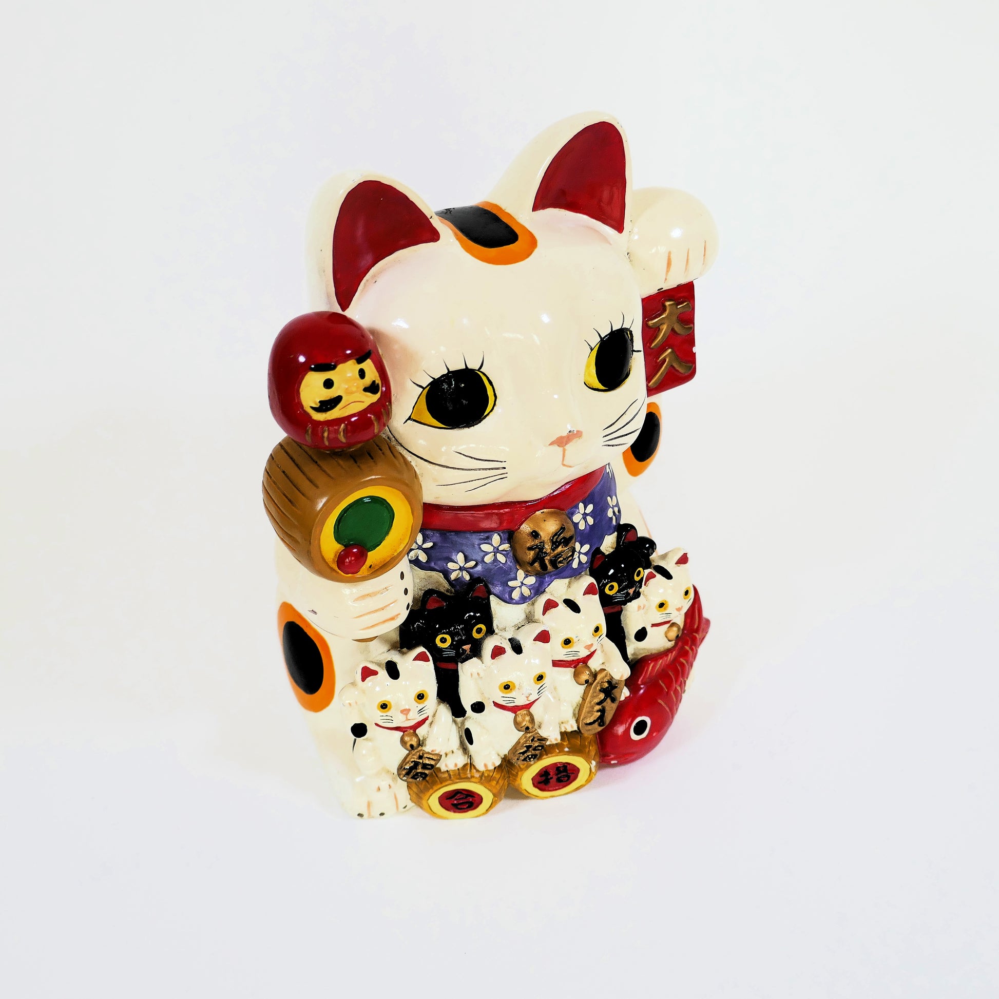 Maneki neko japonais ancien en céramique vu de côté, montrant ses décorations et sa patte levée.