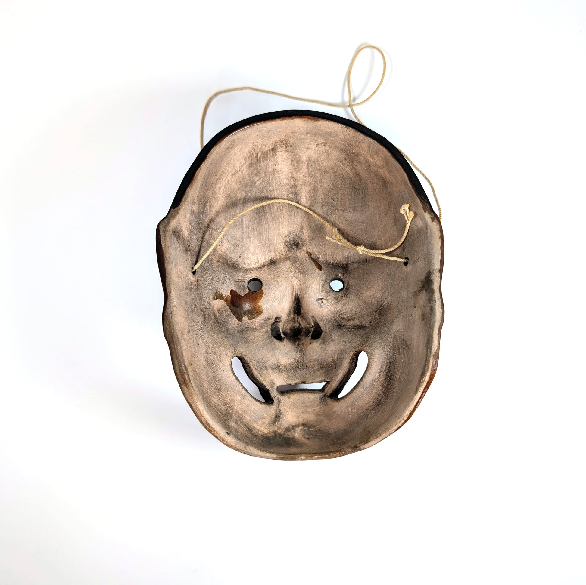 Vue arrière d’un masque de théâtre Nô japonais en céramique, montrant les cordelettes d’attache