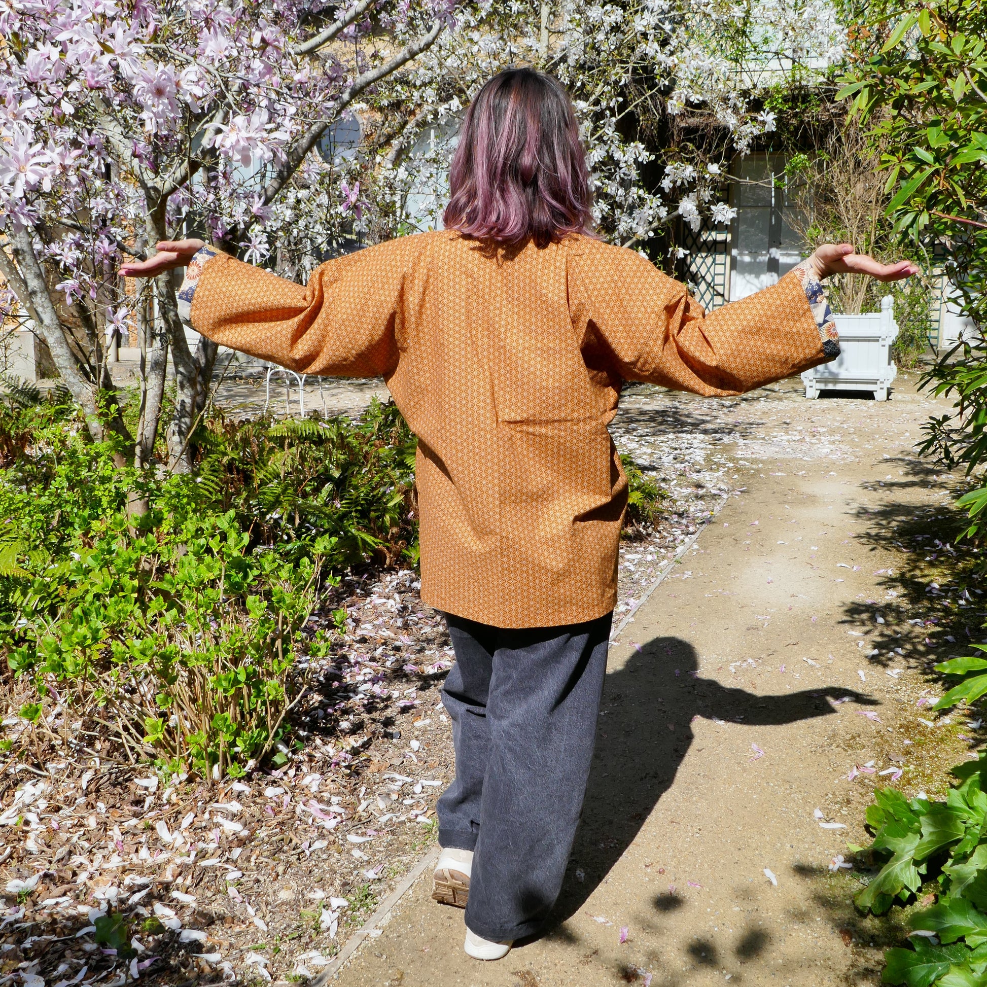 Vue de dos de Mikan en haori Yūyake Zakura, au milieu des pétales tombés au sol.
