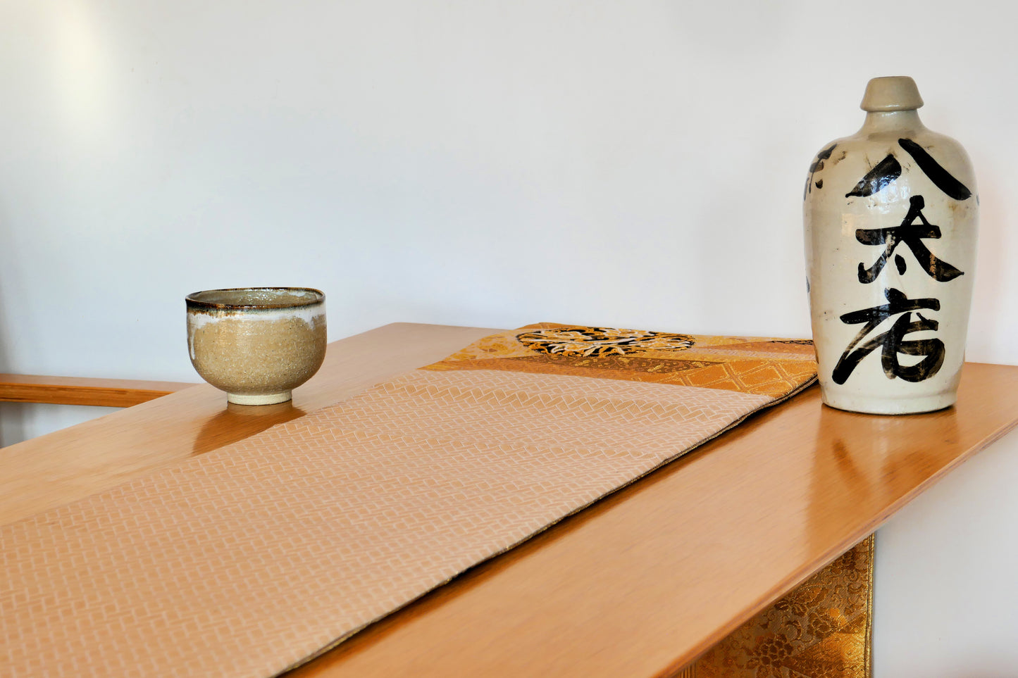 Obi en soie dorée motif chevron, décoré avec bol et bouteille tokuri sur table japonaise