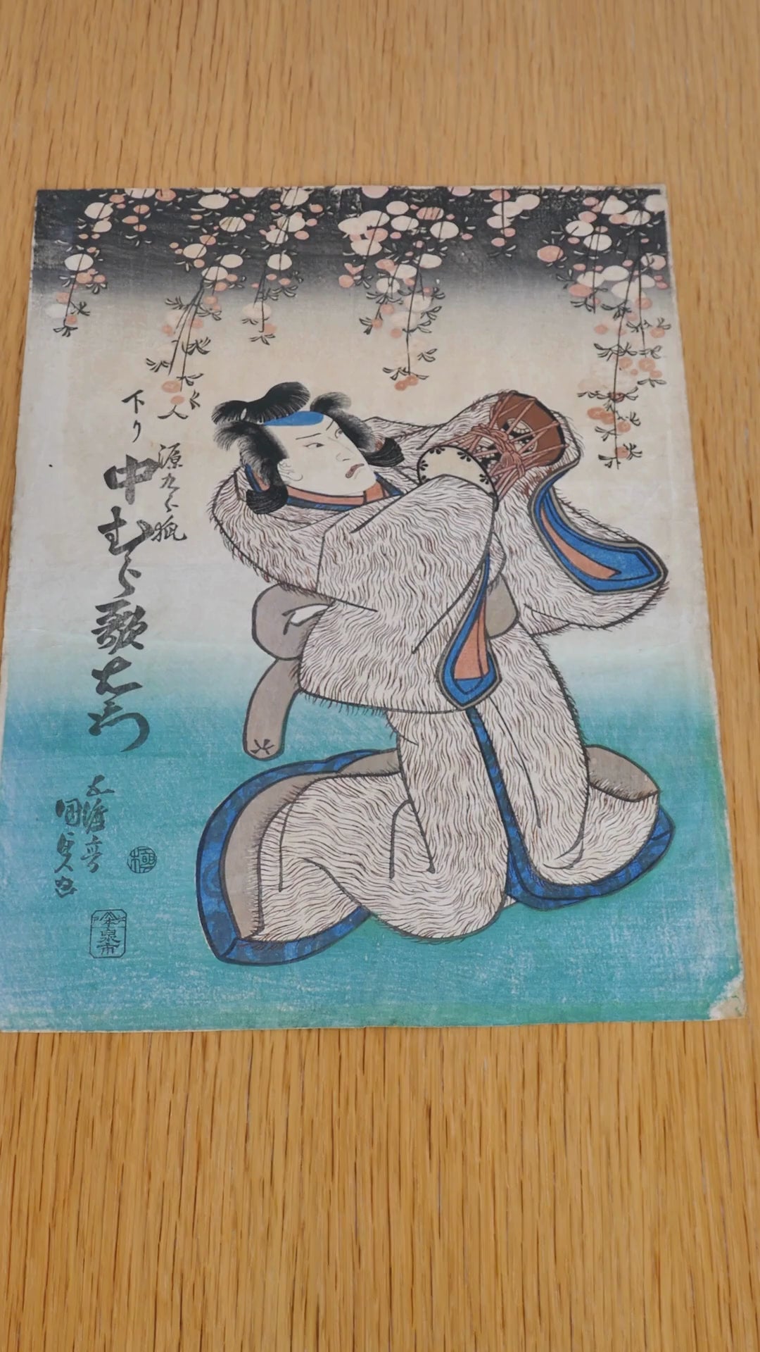 Estampe de 1838 signée Kunisada, représentant l’acteur Nakamura Utaemon dans le rôle du renard Genkurô, issu de la pièce kabuki Yoshitsune Senbon Zakura. Le personnage tient le tambour Hatsune. Détails raffinés : kimono à motif "fourrure", cerisiers pleureurs en fleur, gaufrage karazuri visible. Couleurs patinées, coins abîmés. Belle pièce yakusha-e de la période Edo.