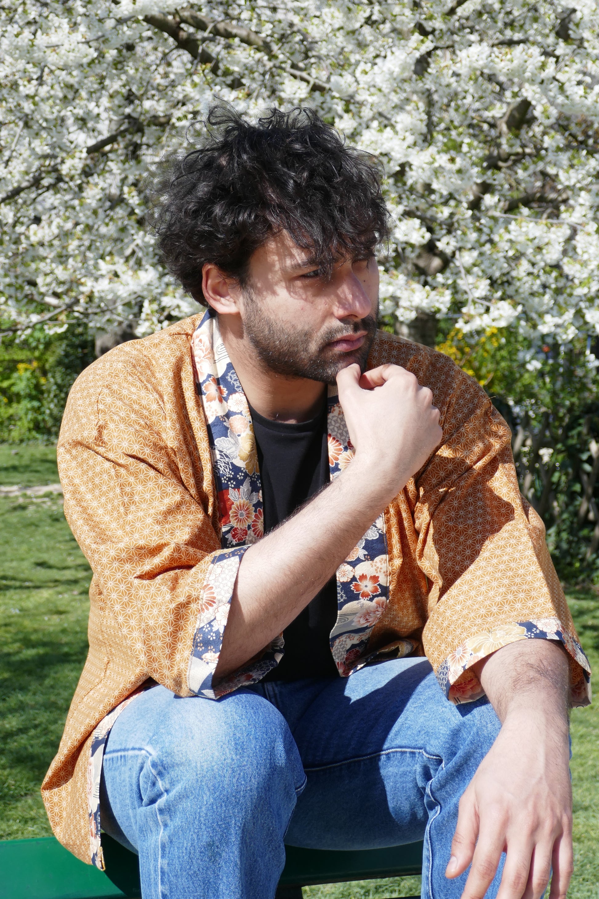 Richard assis, pensif, en haori Yūyake Zakura sous un cerisier en fleurs.