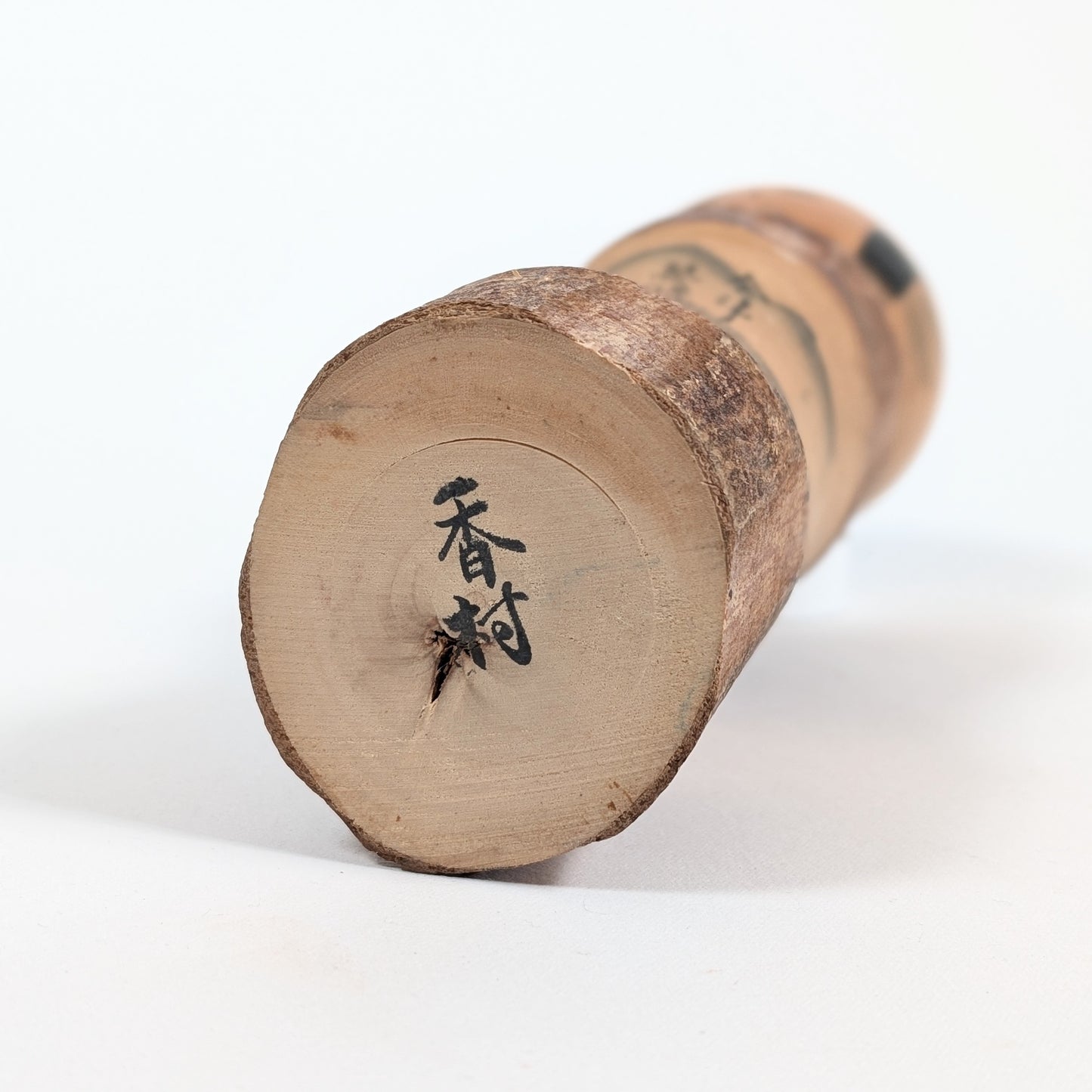 Signature 香村 sous la base d’une kokeshi omiyage japonaise en bois, œuvre de Sato Kôson 佐藤香村, artisane de Fukushima.