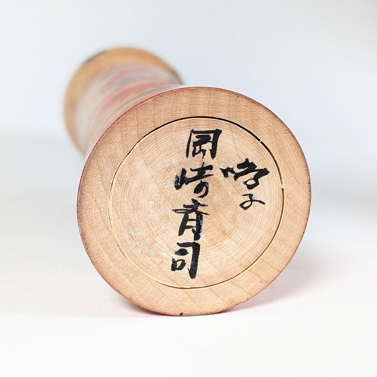 Signature 岡崎斉司 sous la base d’une kokeshi Naruko d’Okazaki Seishi, artisan japonais de la tradition des kokeshi du Tohoku.