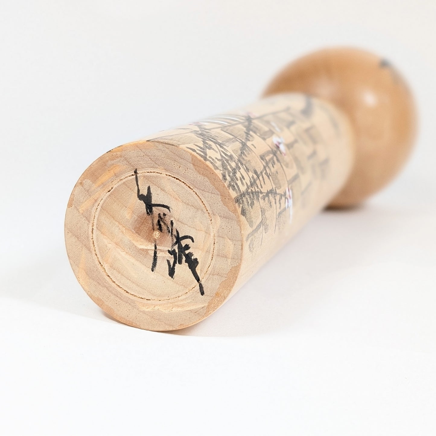 Signature de l’artisan Shūhō 秀峰 sous la base de la kokeshi japonaise en bois, vue rapprochée.