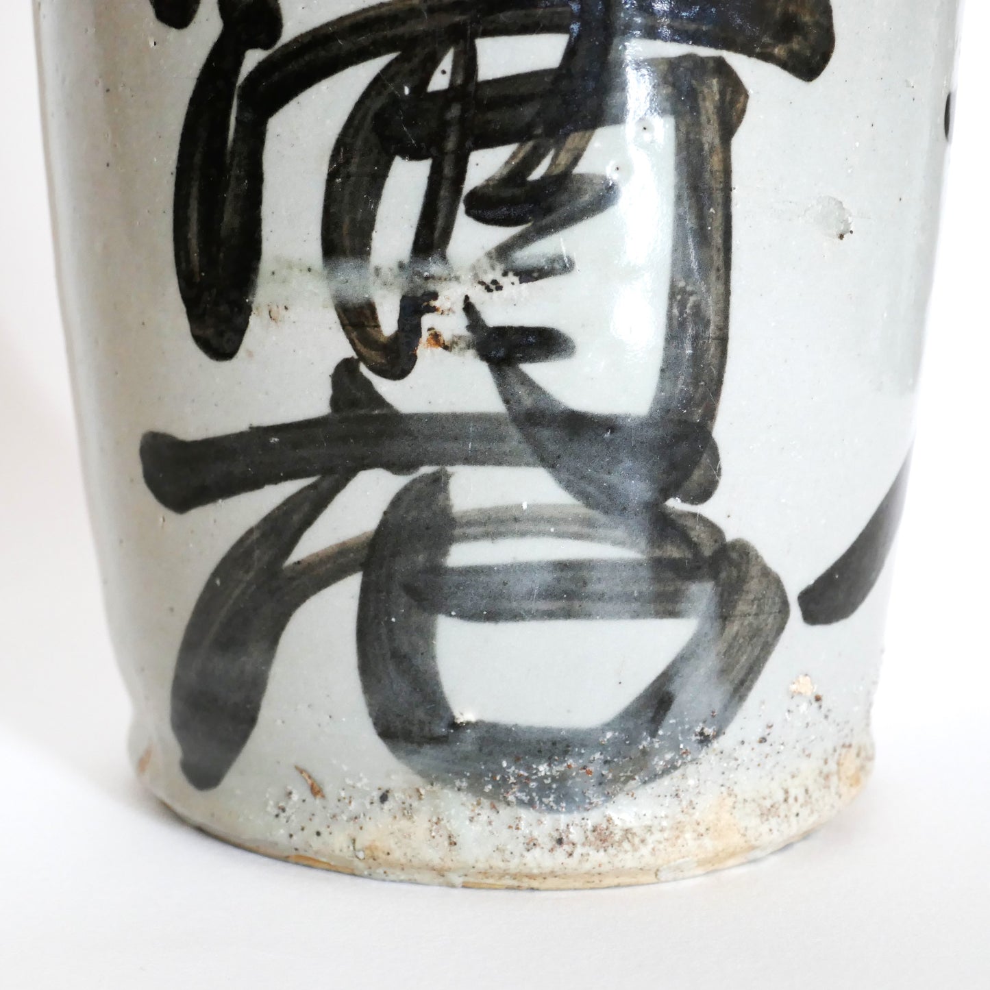 Gros plan sur la base d’un tokkuri japonais vintage de l’ère Shōwa, avec calligraphie artisanale en noir sur grès clair