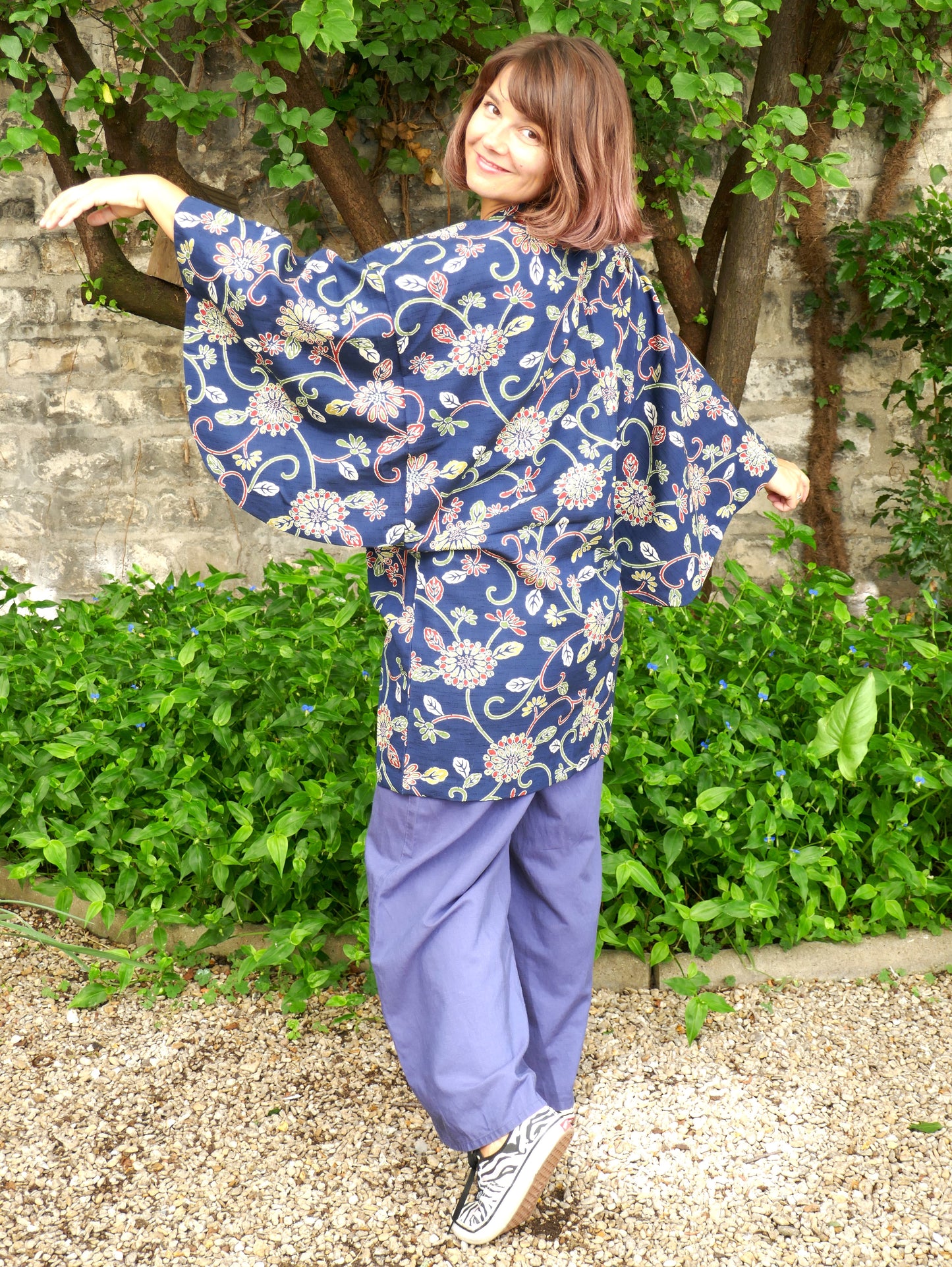 Mikan virevoltant joyeusement en dochugi japonais vintage, à motif floral sur fond bleu. Veste kimono croisée, ample et confortable, idéale pour une tenue bohème chic d’inspiration japonaise.