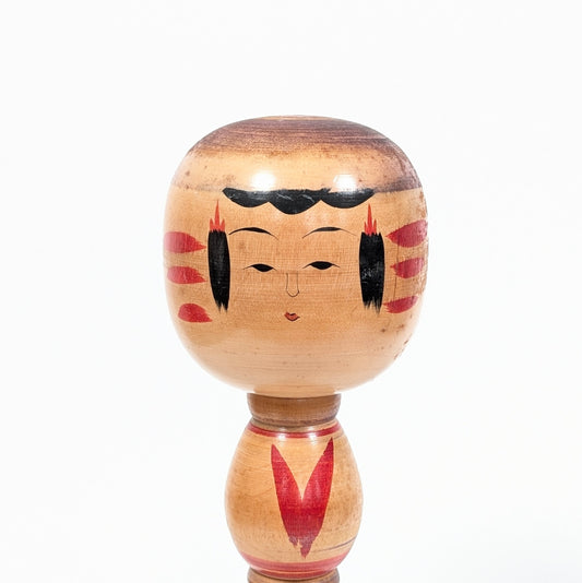 Détail du visage peint d’une kokeshi Ogura Katsushi, avec coiffure noire, ornements rouges et grain naturel du bois