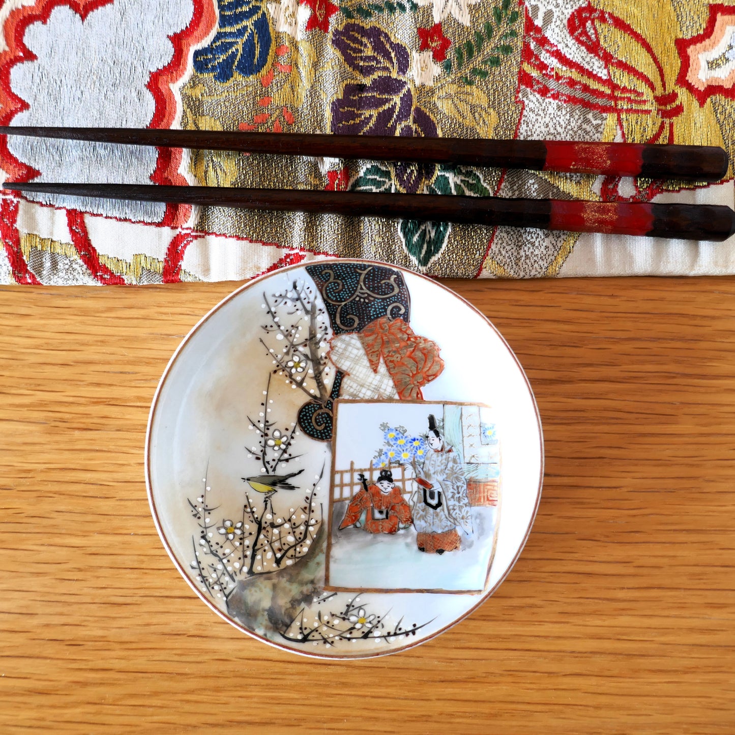 Assiette Kutani vue du dessus, accompagnée de baguettes et d’un tissu japonais coloré