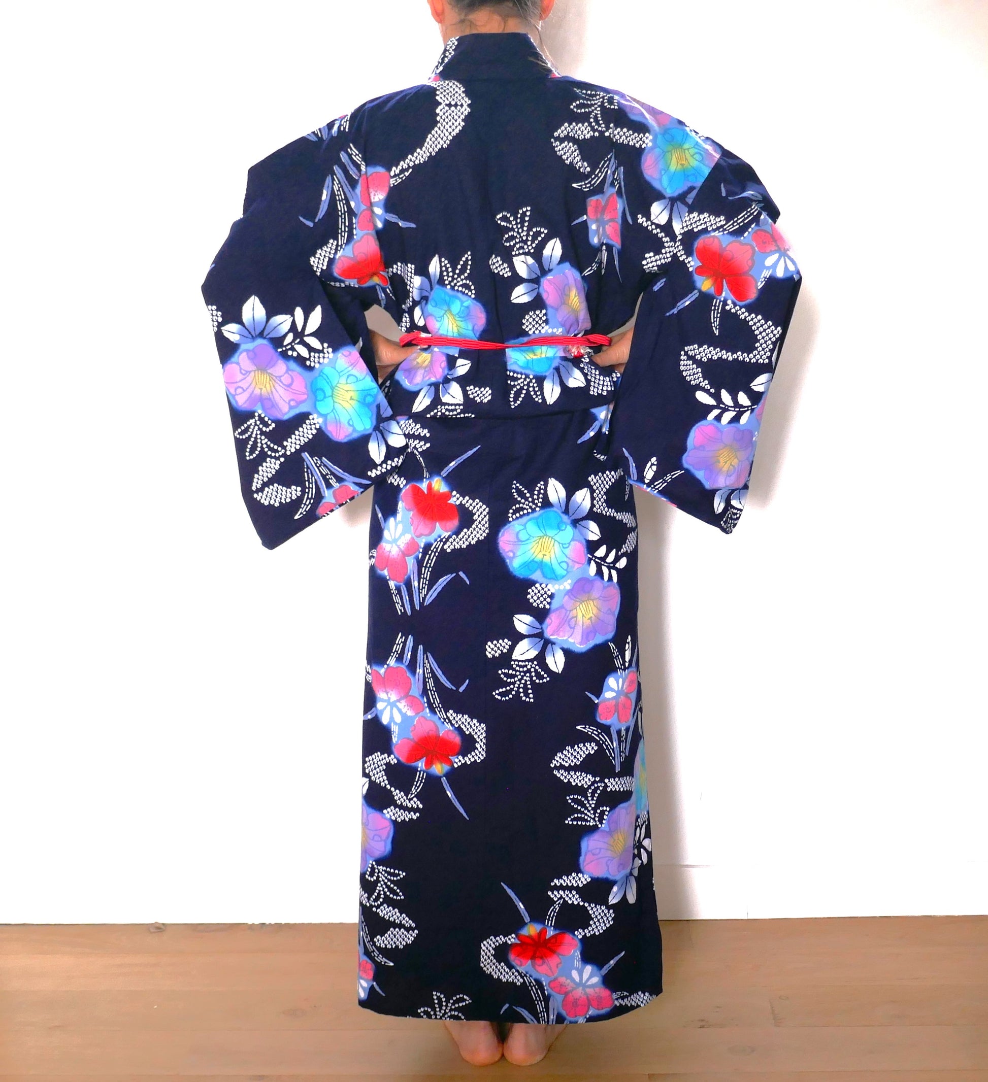 Dos d’un yukata en coton fleuri bleu marine porté avec ceinture obijime rouge.