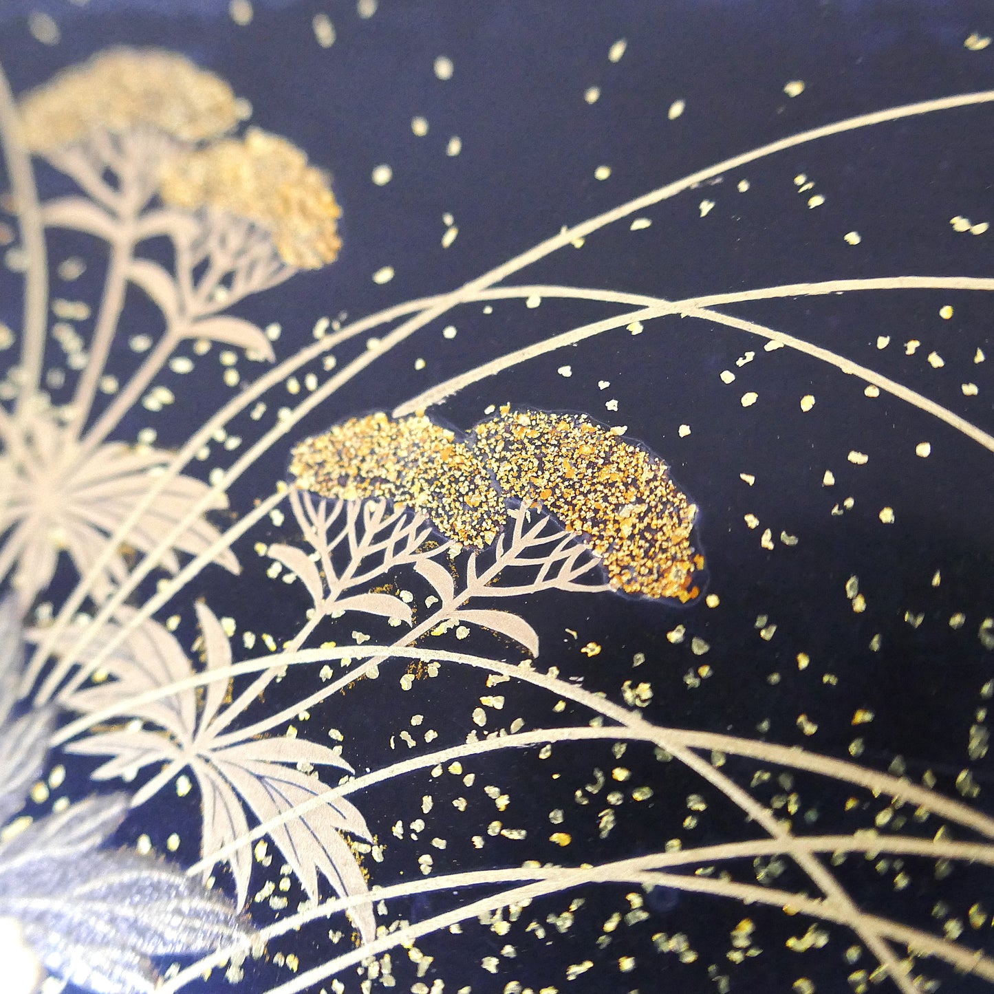 Zoom sur décor floral doré en maki-e sur boîte japonaise traditionnelle Zohiko, détails d’herbes et fleurs.