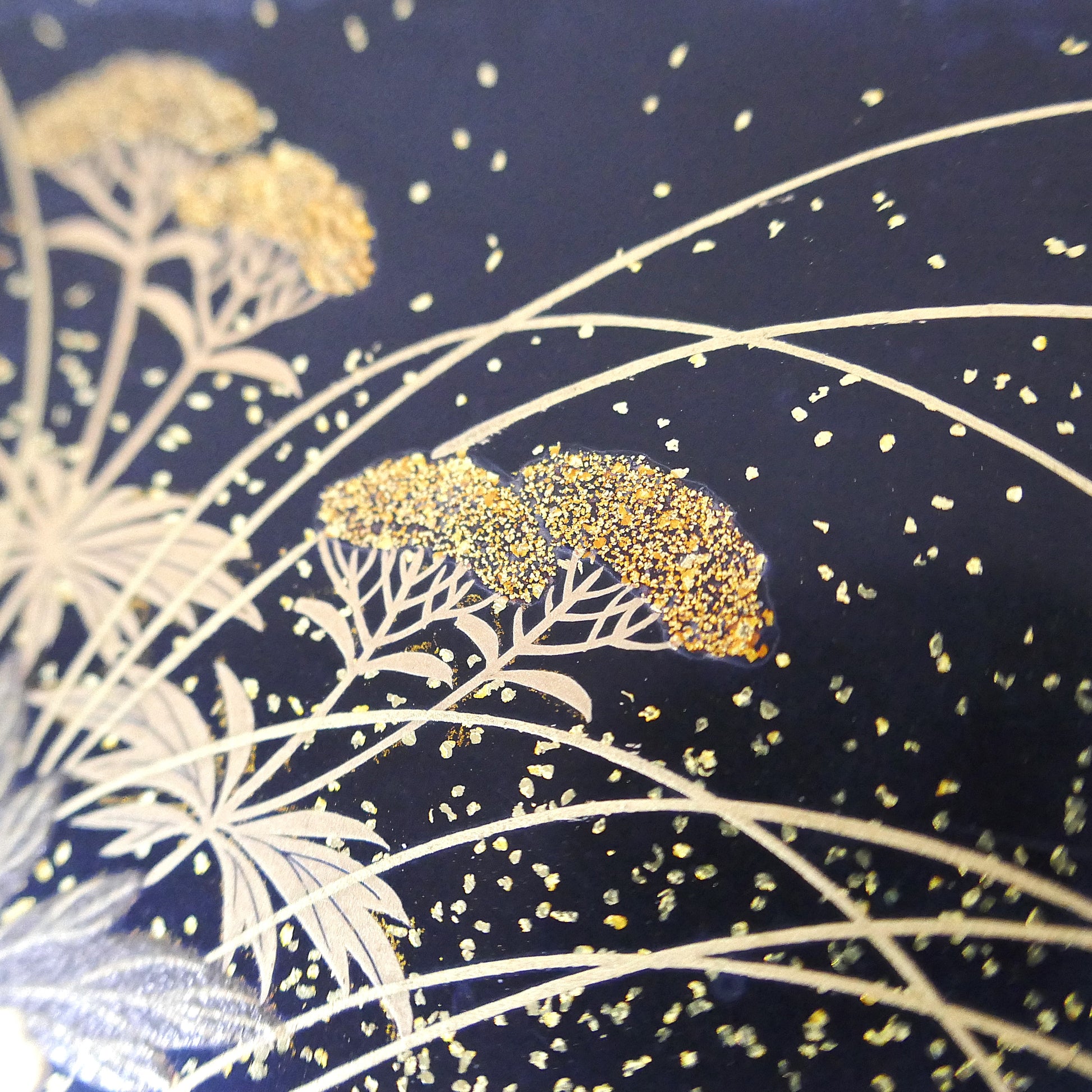 Zoom sur décor floral doré en maki-e sur boîte japonaise traditionnelle Zohiko, détails d’herbes et fleurs.