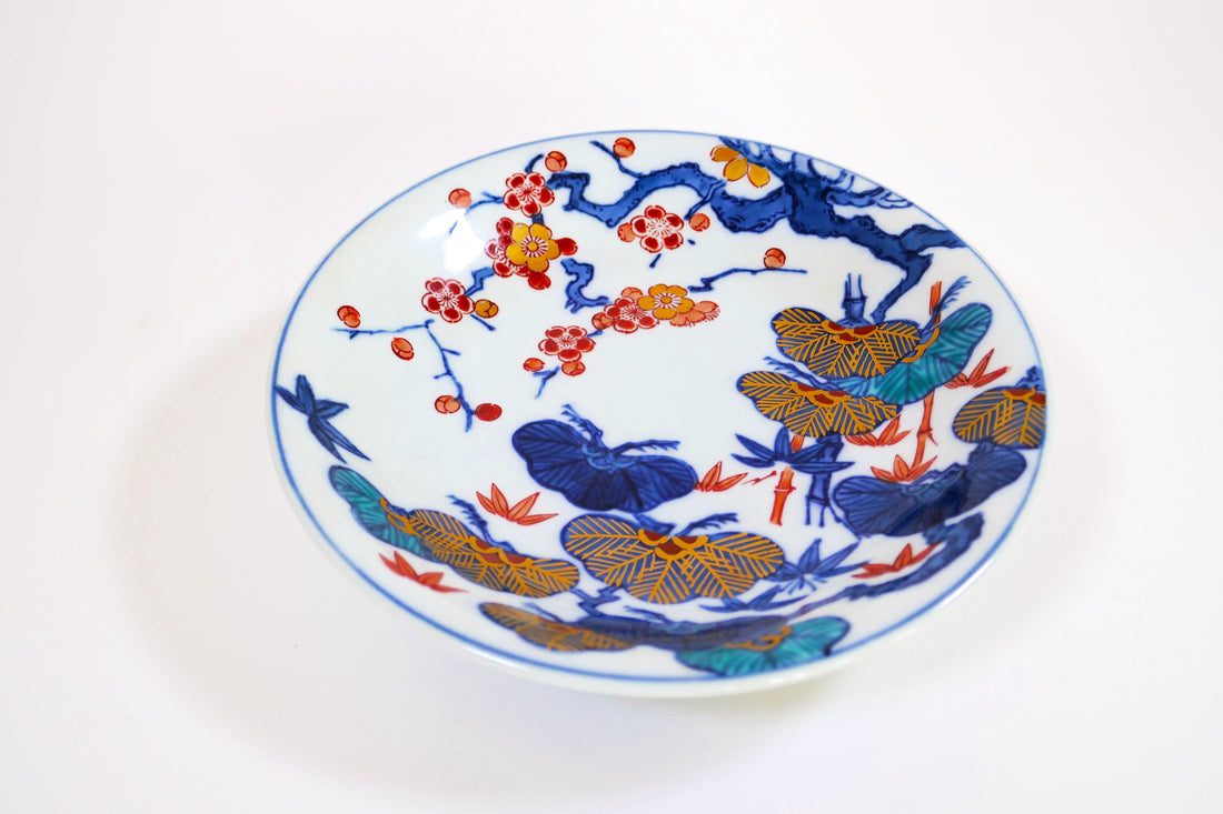 Assiette ancienne en porcelaine japonaise de style Arita, décorée de branches de prunier en fleurs et de papillons colorés sur fond blanc