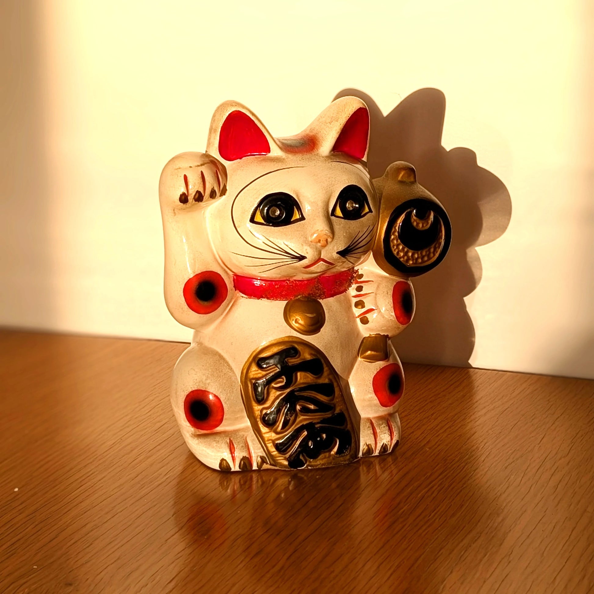 Maneki-neko vintage en céramique dans la lumière du soleil, chat japonais porte-bonheur avec marteau à vœux et plaque de prospérité.