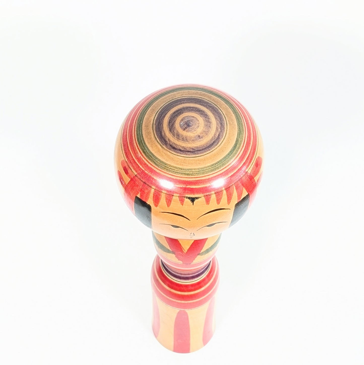 Sommet de tête d’une kokeshi Yajirō avec cercles concentriques rouges, verts et violets Janome, détail typique des poupées kokeshi traditionnelles japonaises