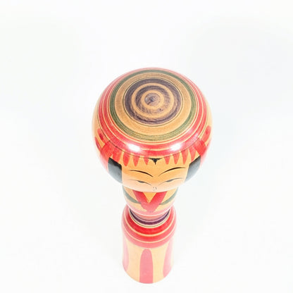Sommet de tête d’une kokeshi Yajirō avec cercles concentriques rouges, verts et violets Janome, détail typique des poupées kokeshi traditionnelles japonaises