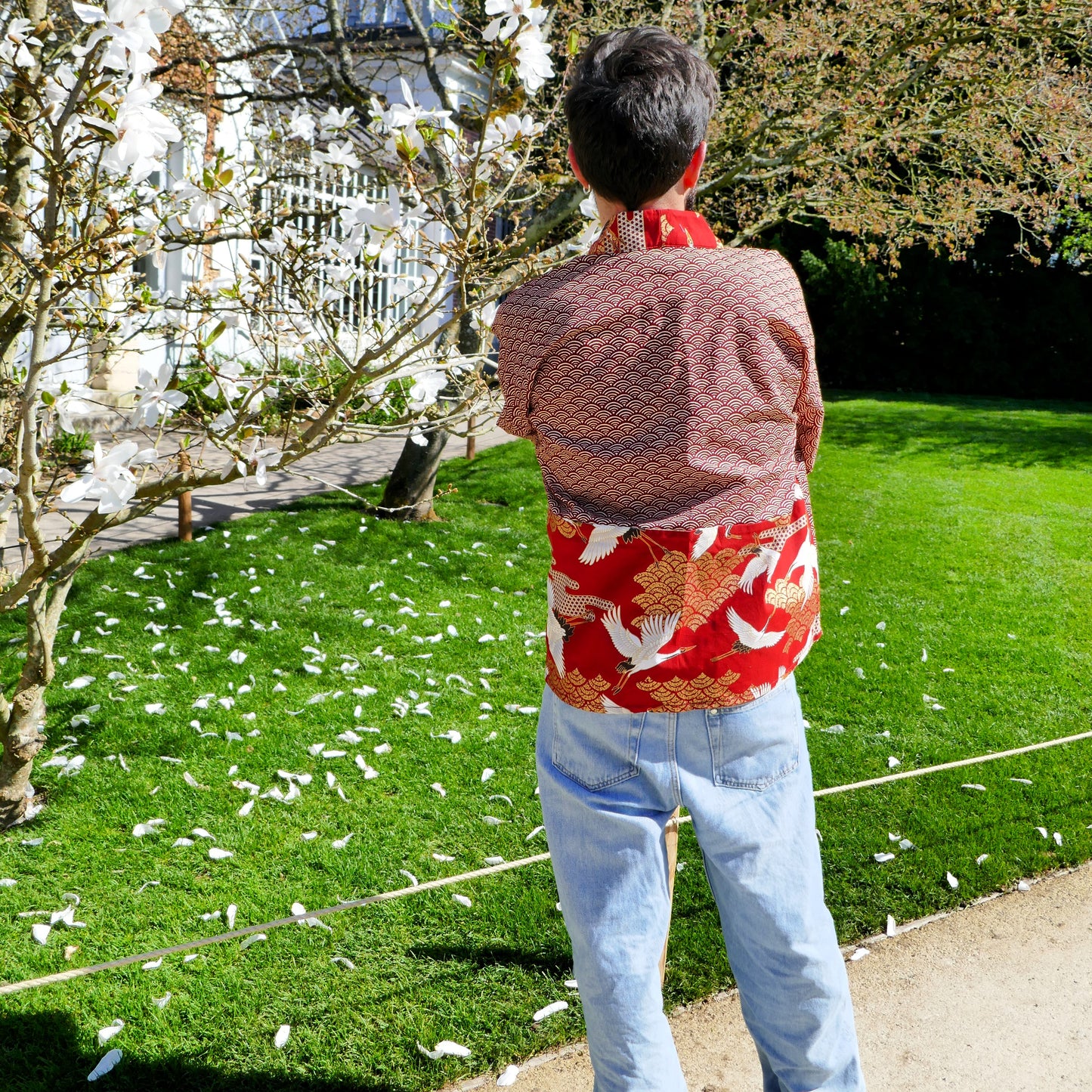  Dos du haori Akane Tsuru porté par Tôma, mettant en valeur les motifs de grues blanches sur fond rouge intense et or.