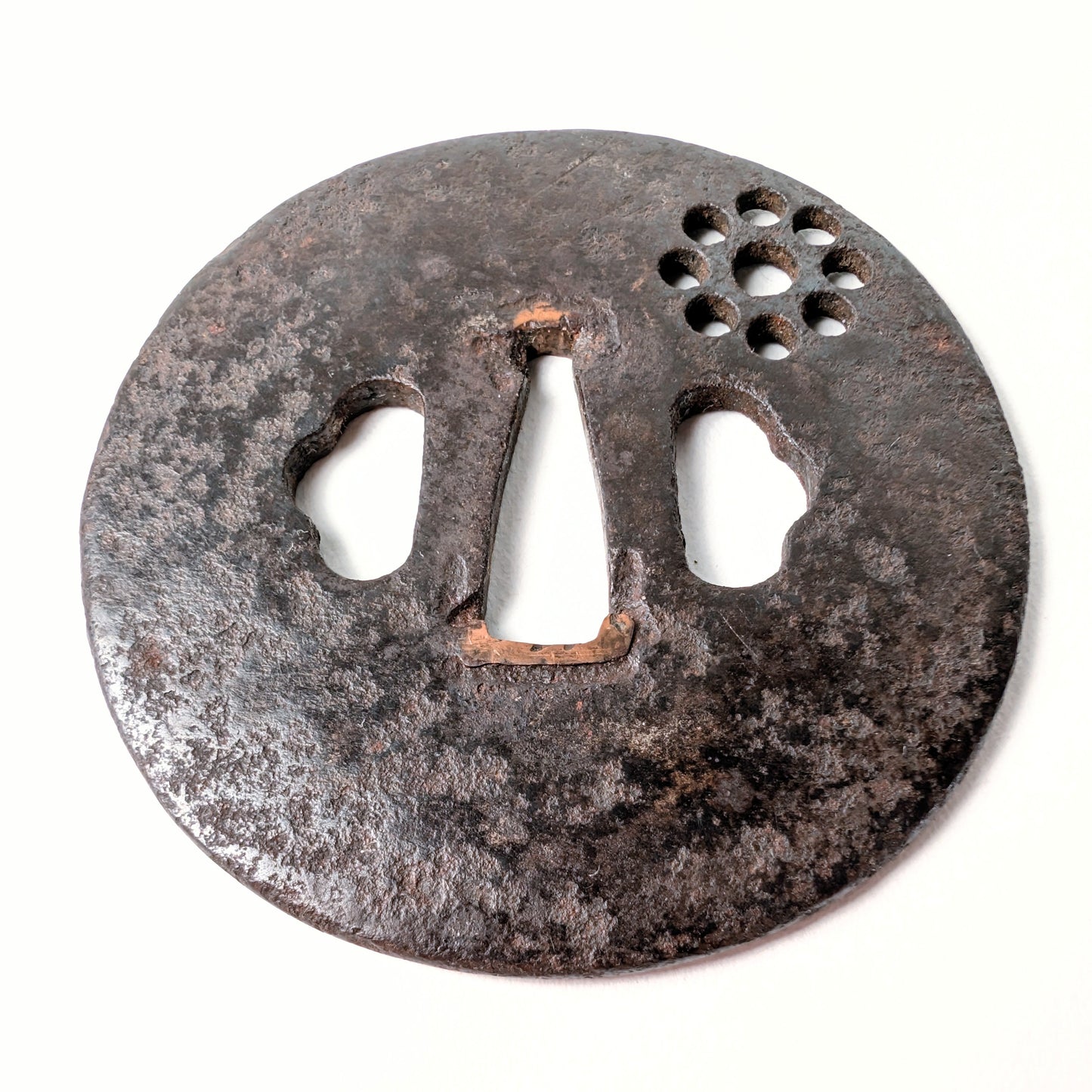 Vue oblique d’une ancienne tsuba de samouraï en fer, avec motif symbolique Kuyō des Neuf Astres en décor ajouré.