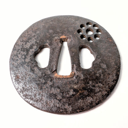 Vue oblique d’une ancienne tsuba de samouraï en fer, avec motif symbolique Kuyō des Neuf Astres en décor ajouré.