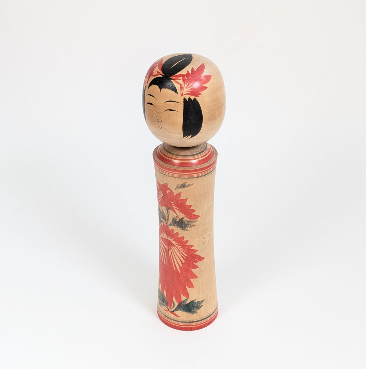 Kokeshi traditionnelle du Japon vue de trois-quarts, style Naruko et décor de chrysanthème hishigiku peint en rouge et noir.