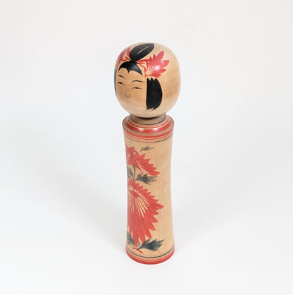 Kokeshi traditionnelle du Japon vue de trois-quarts, style Naruko et décor de chrysanthème hishigiku peint en rouge et noir.
