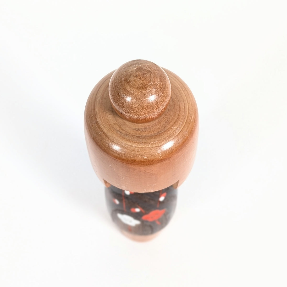 Vue de dessus de la coiffure en bois tourné d'une kokeshi artisanale Usaburo, avec un chignon sphérique et des cercles de croissance visibles dans le bois clair.
