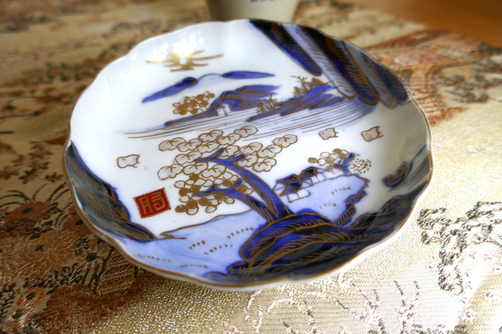 Gros plan sur le décor doré de paysage japonais et le sceau rouge Hizen sur assiette Meiji