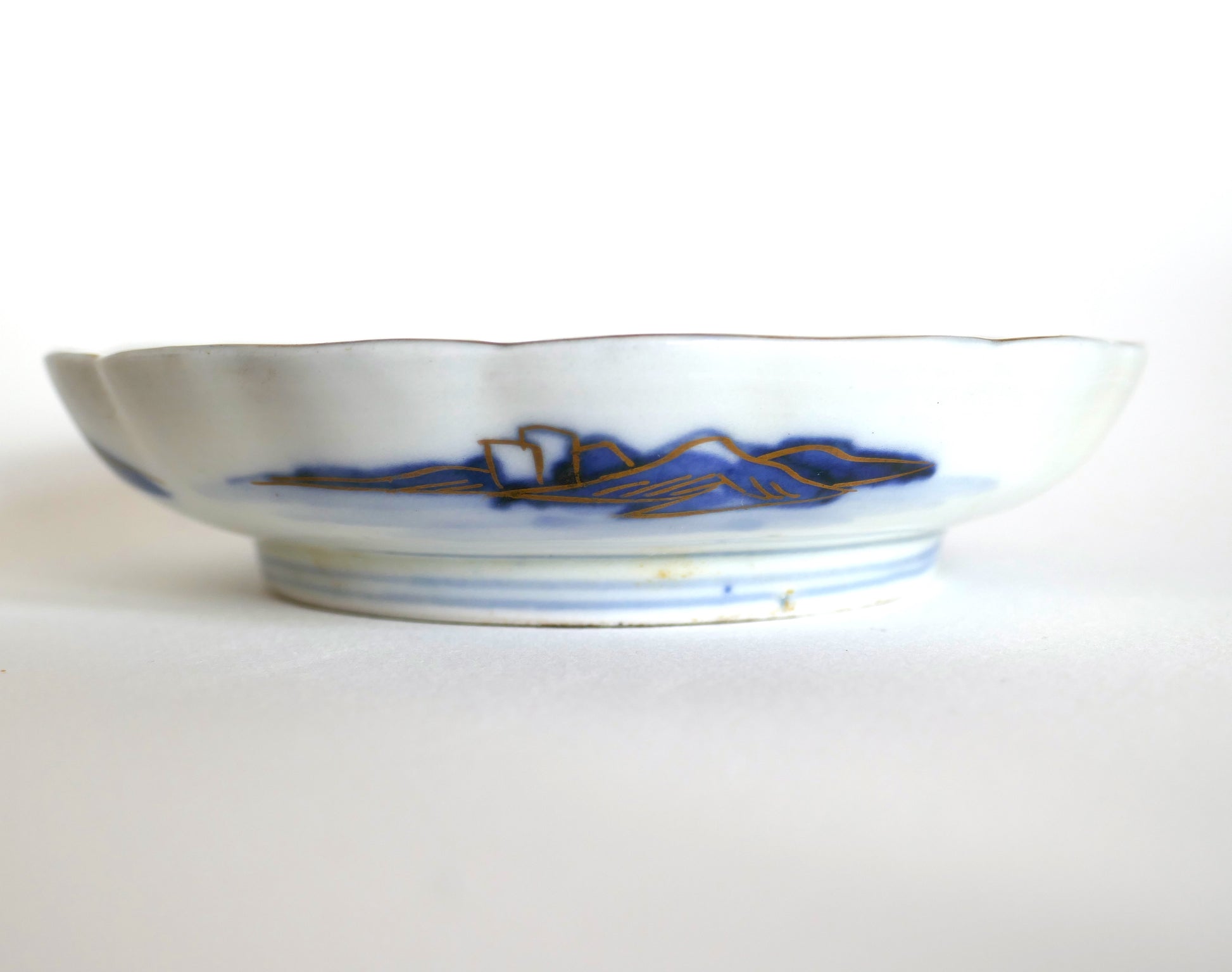 Vue latérale d’une assiette Arita Meiji montrant le décor extérieur de montagnes bleues et dorures