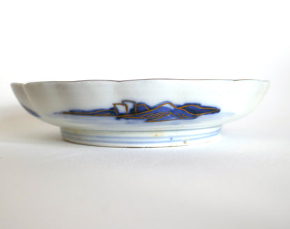 Vue latérale d’une assiette Arita Meiji montrant le décor extérieur de montagnes bleues et dorures