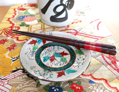 Petite assiette japonaise Inuyama-yaki de l’époque Edo, décorée de feuilles d’érable rouges et vertes sur fond craquelé. Présentée avec des baguettes en bois laqué rouge sur un obi brodé aux motifs floraux dorés et une bouteille de saké calligraphiée.