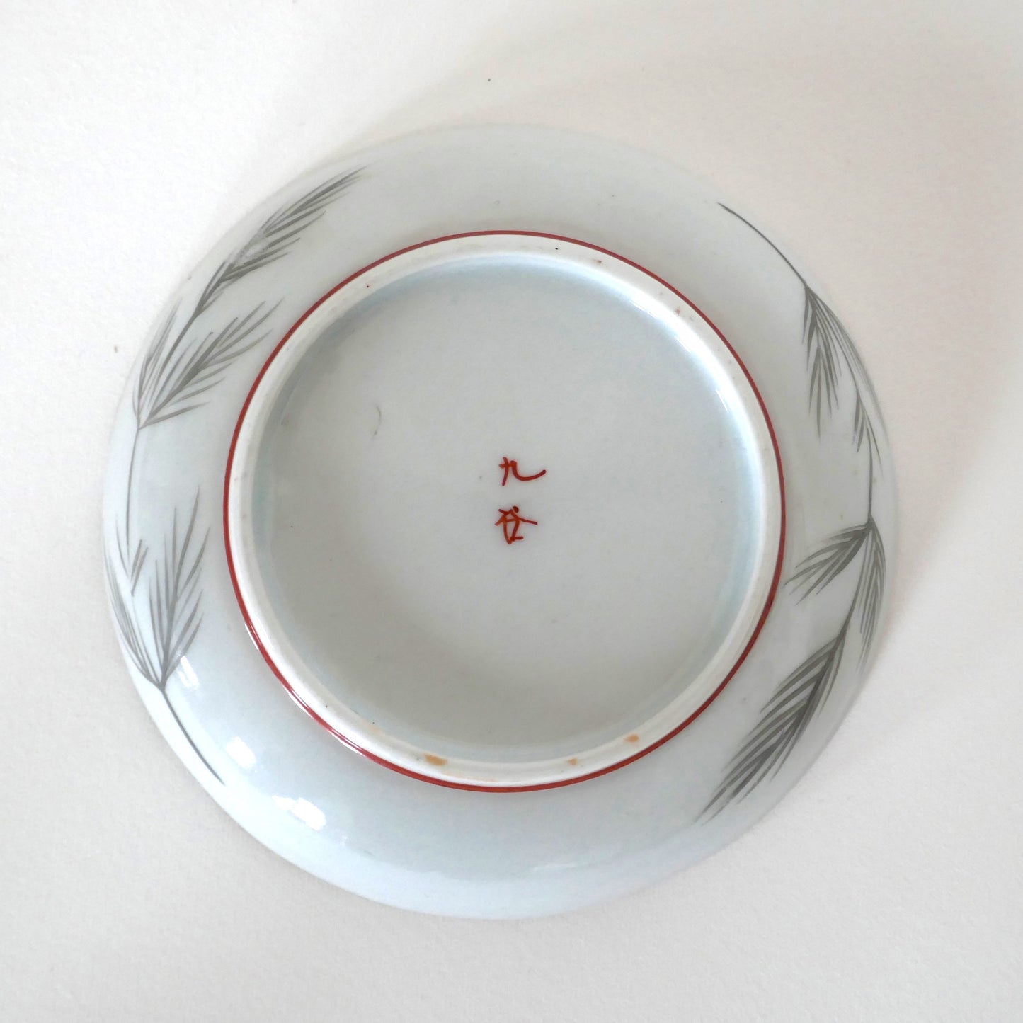 Vue du dessous de l’assiette Kutani avec signature 九谷 et décor de branches de pin