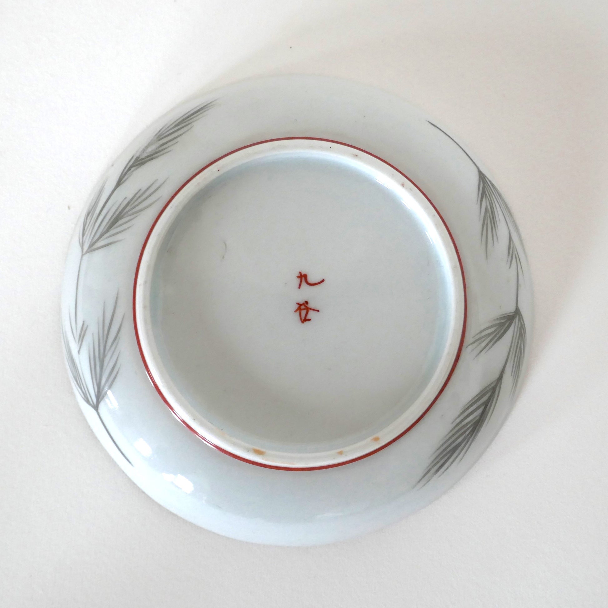 Vue du dessous de l’assiette Kutani avec signature 九谷 et décor de branches de pin