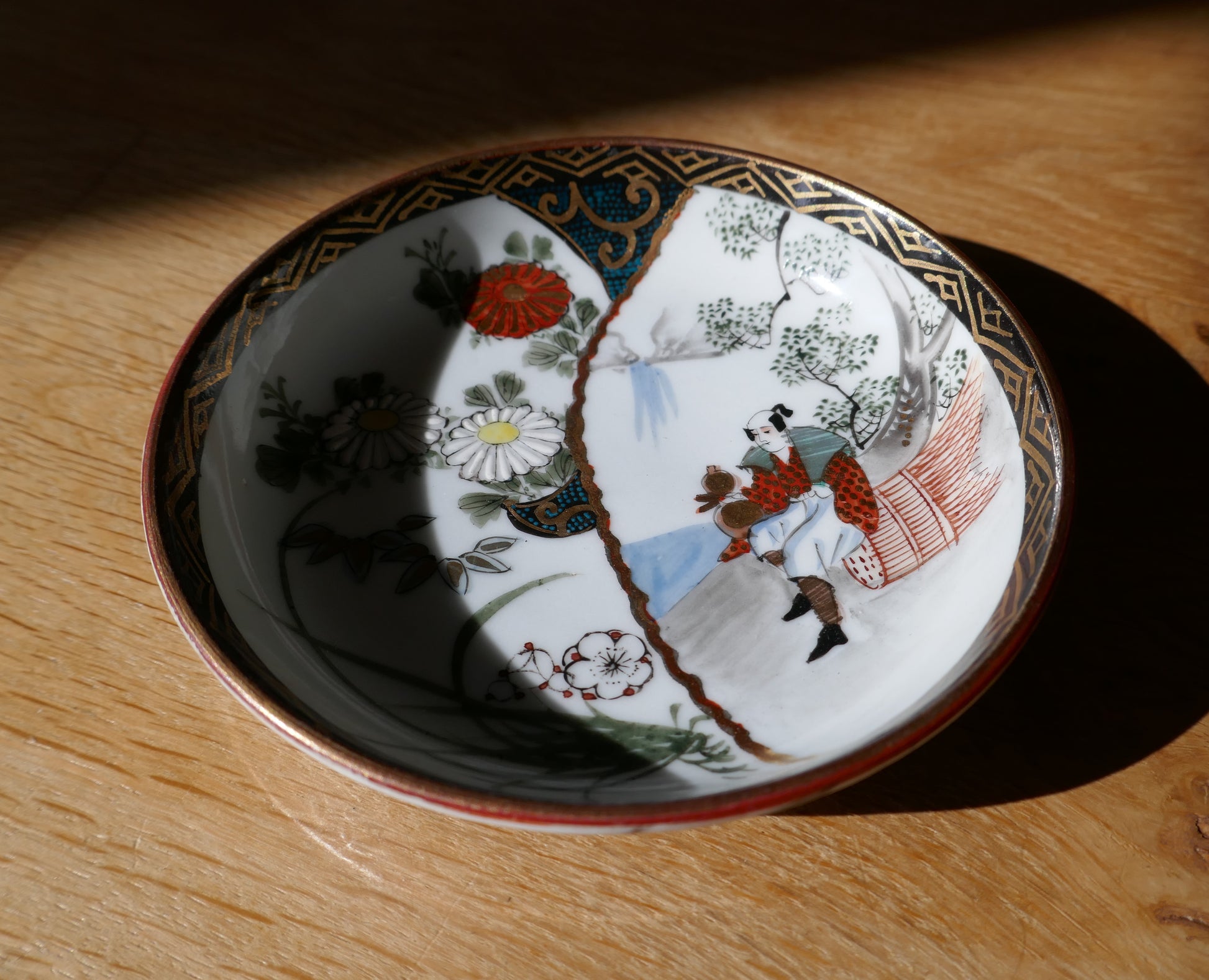 Vue de dessus d’une assiette Kutani décorée d’un personnage, de chrysanthèmes et motifs floraux japonais