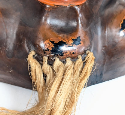 Gros plan sur la barbe en fibres végétales d’un masque japonais de Daikoku et sur la finition rouge-noir du menton.