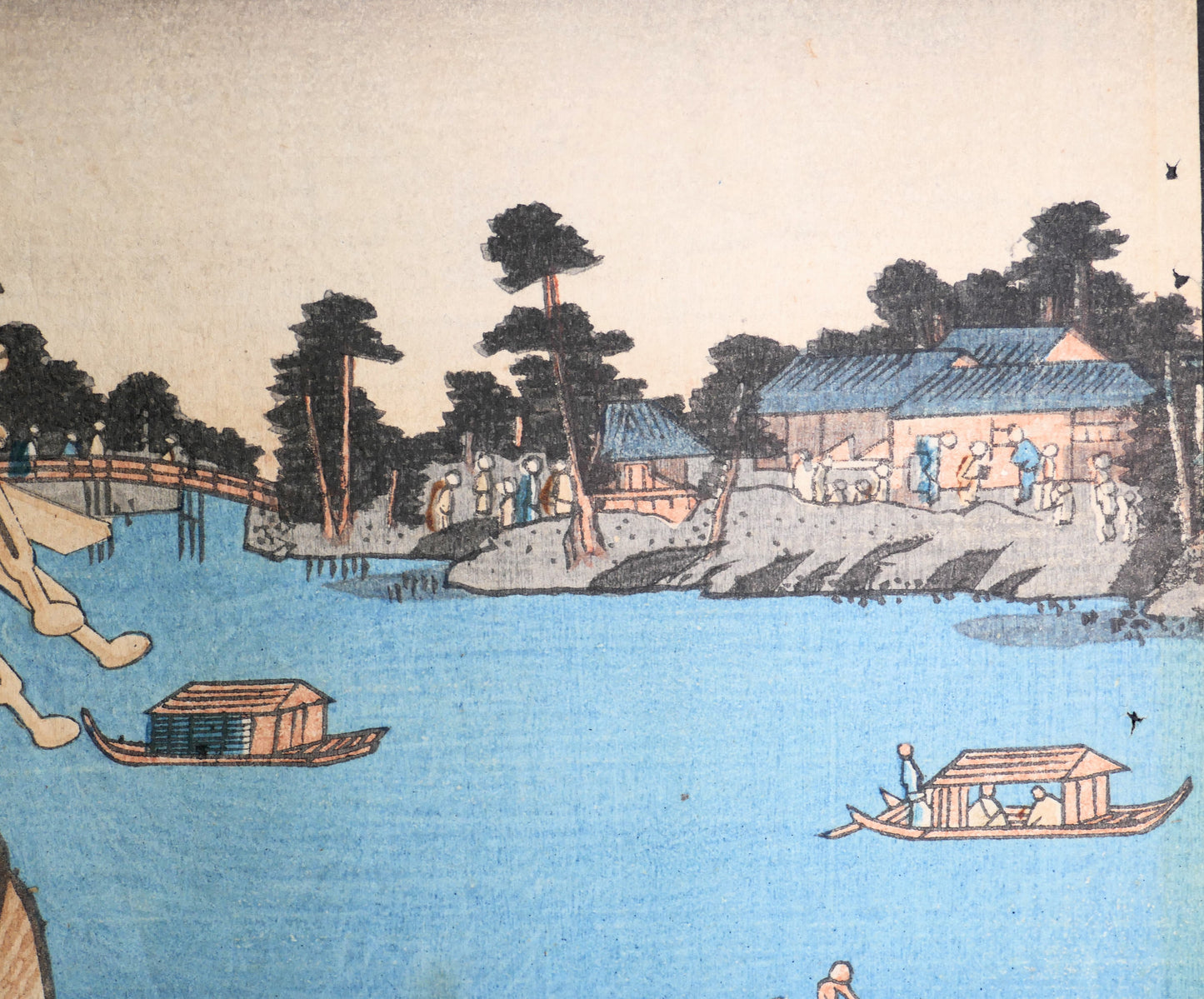 Détail du décor au bord de l’eau avec bateaux japonais, pont, maisons et silhouettes, sur une estampe ukiyo-e de Kunisada datée de 1856.