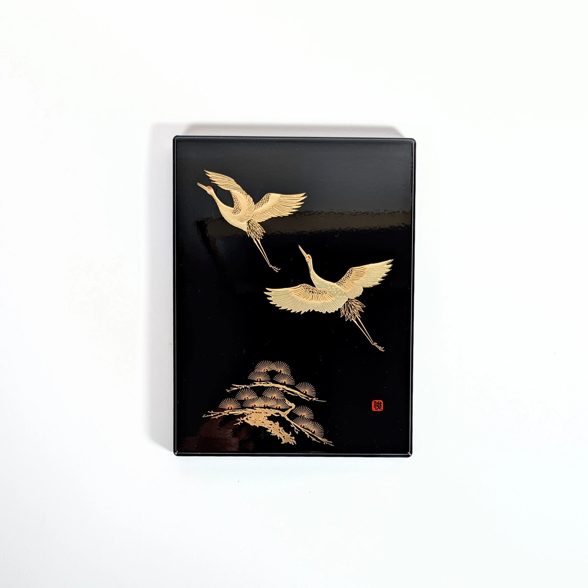 Boîte japonaise laquée noire, décor de grues dorées et pin stylisé, vue de face.