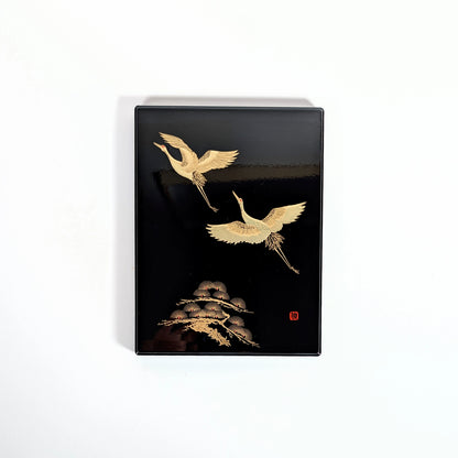 Boîte japonaise laquée noire, décor de grues dorées et pin stylisé, vue de face.