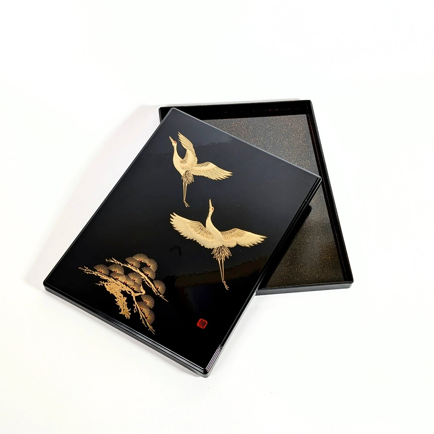 Boîte japonaise en laque urushi noire, décor de grues dorées, vue avec couvercle posé sur le plateau.