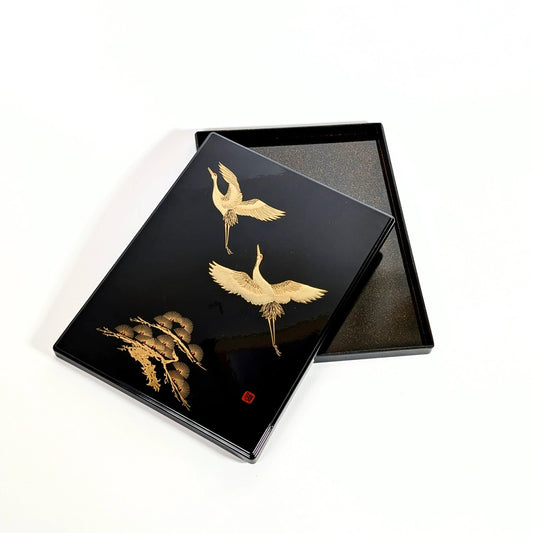 Boîte japonaise en laque urushi noire, décor de grues dorées, vue avec couvercle posé sur le plateau.