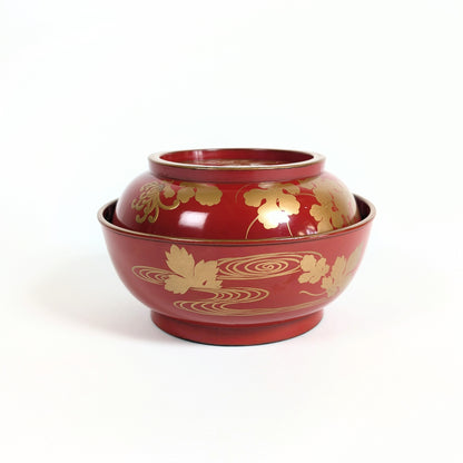 Vue de face d’un bol japonais avec couvercle en laque urushi rouge et décor doré de chrysanthèmes et cours d’eau.