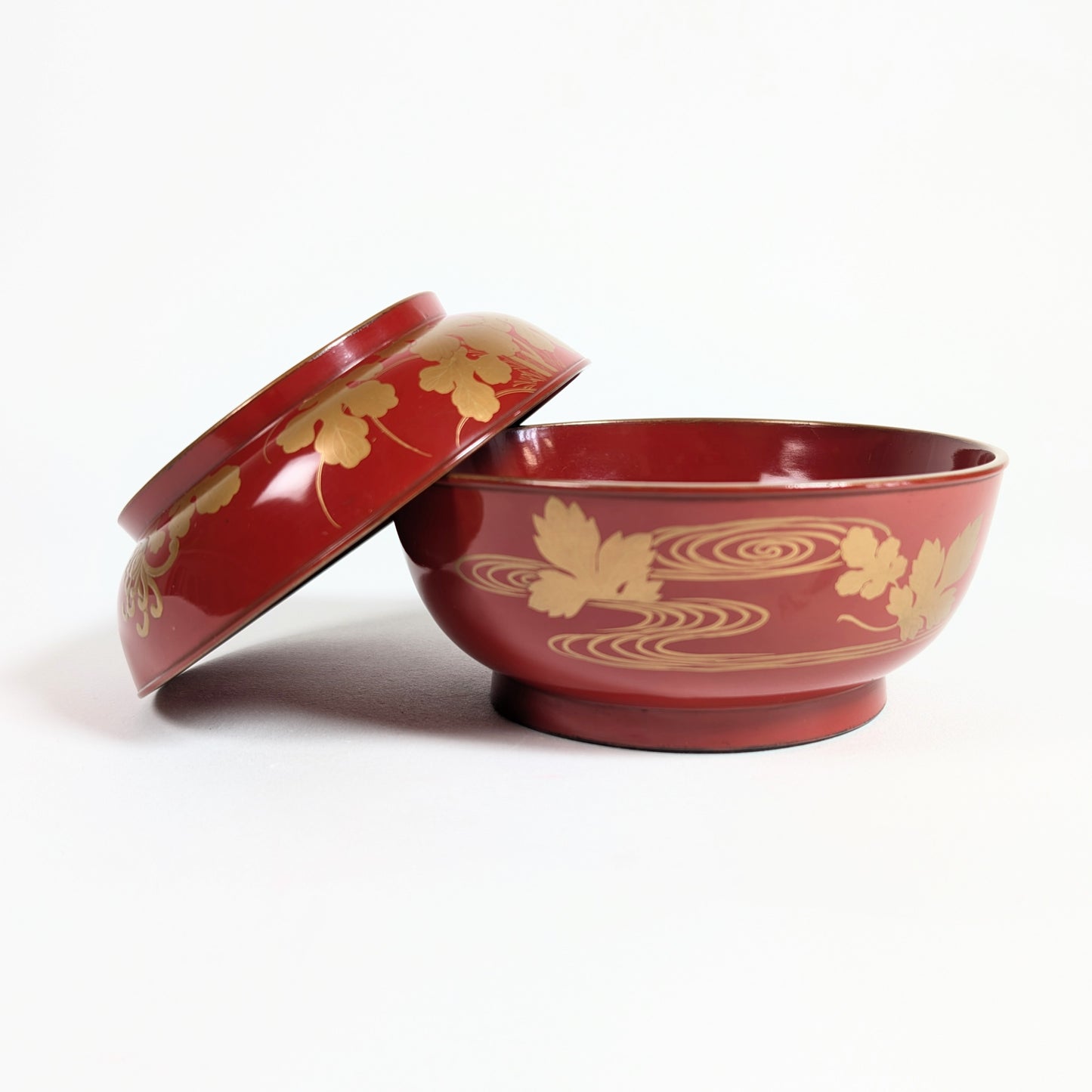 Bol japonais ancien en laque rouge présenté ouvert avec son couvercle, décor doré de chrysanthèmes et eaux stylisées.