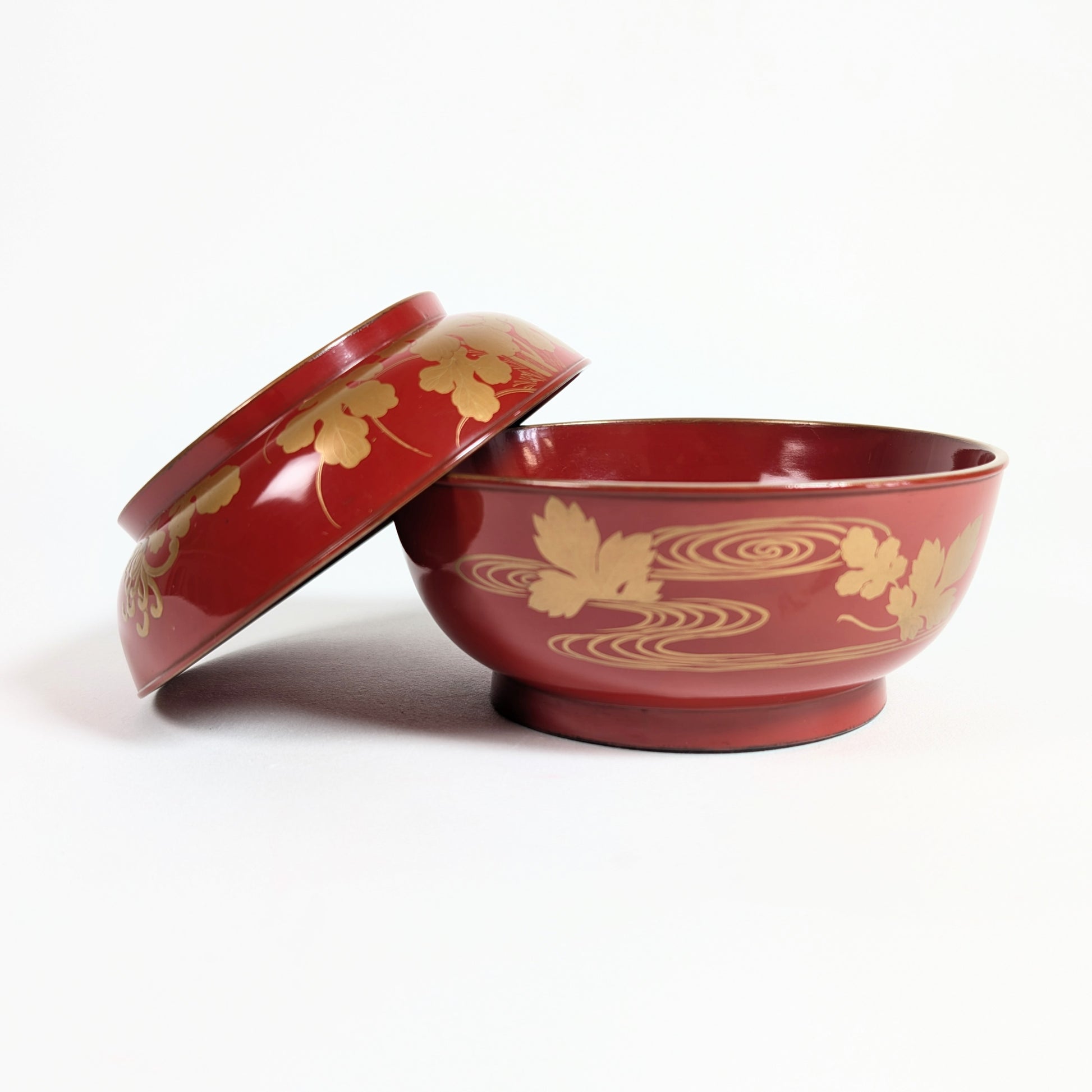 Bol japonais ancien en laque rouge présenté ouvert avec son couvercle, décor doré de chrysanthèmes et eaux stylisées.