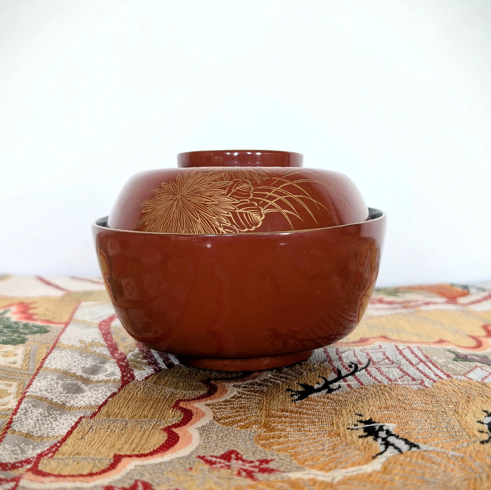 Bol japonais ancien en laque vermillon décoré en maki-e de chrysanthèmes et herbes susuki, posé sur un obi japonais brodé