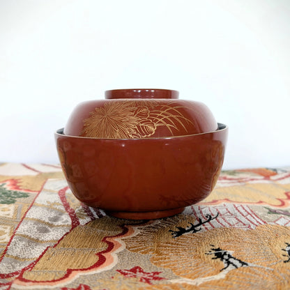 Bol japonais ancien en laque vermillon décoré en maki-e de chrysanthèmes et herbes susuki, posé sur un obi japonais brodé