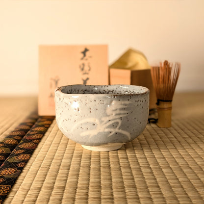Bol à matcha japonais artisanal Nezumi-Shino mis en scène avec chasen et tomobako pour la cérémonie du thé chanoyu.