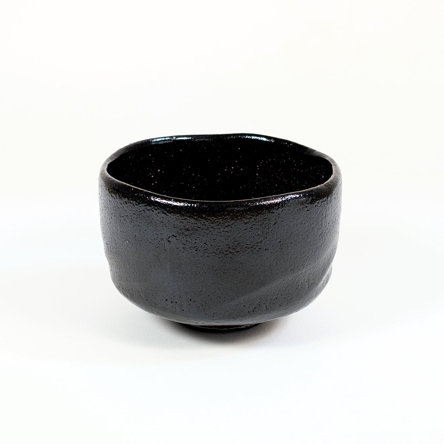 Bol à matcha japonais authentique en raku noir, façonné à la main avec une forme cylindrique et un bord irrégulier.
