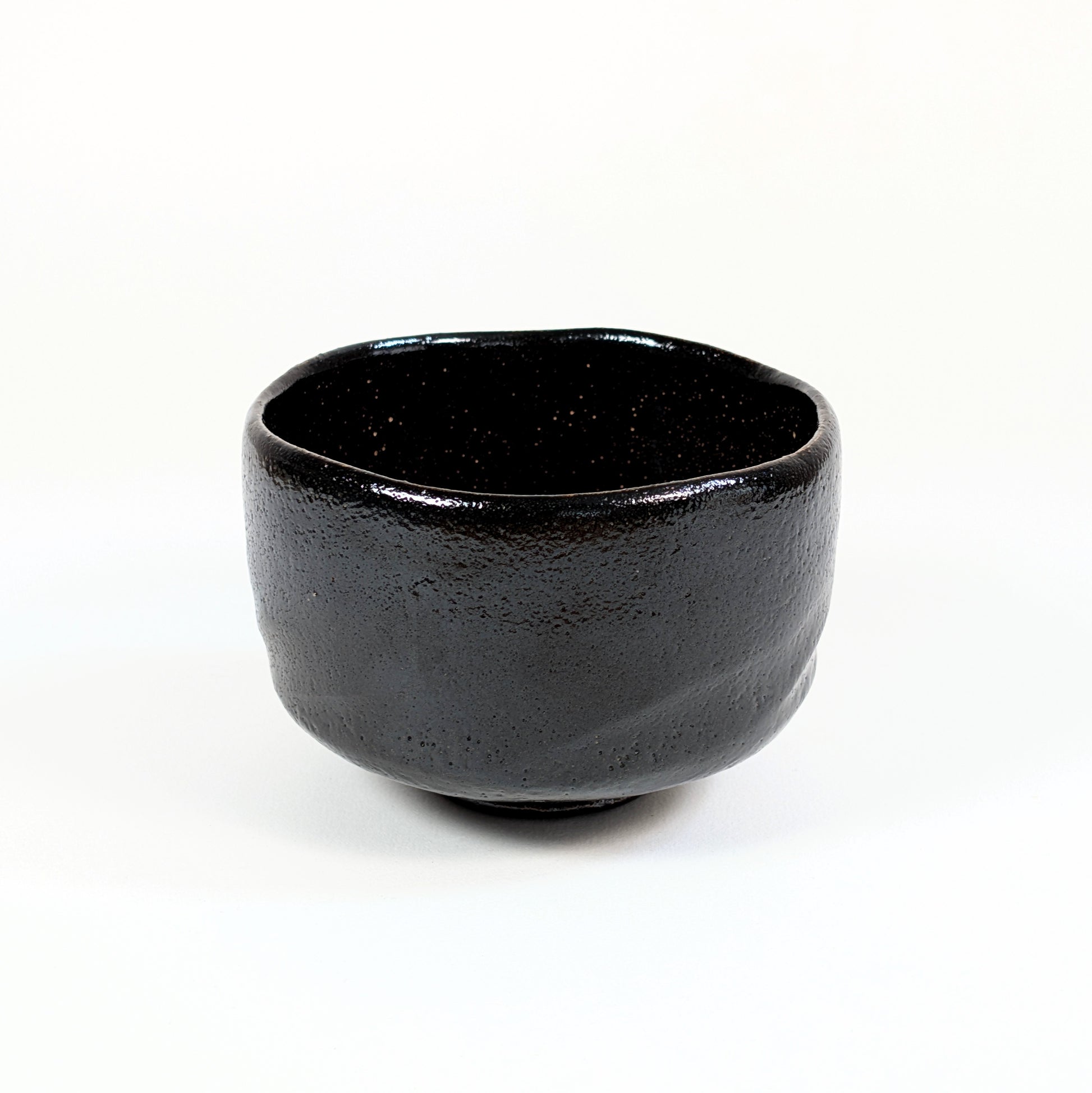 Bol à matcha japonais authentique en raku noir, façonné à la main avec une forme cylindrique et un bord irrégulier.
