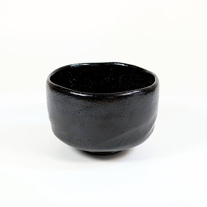 Bol à matcha japonais authentique en raku noir, façonné à la main avec une forme cylindrique et un bord irrégulier.
