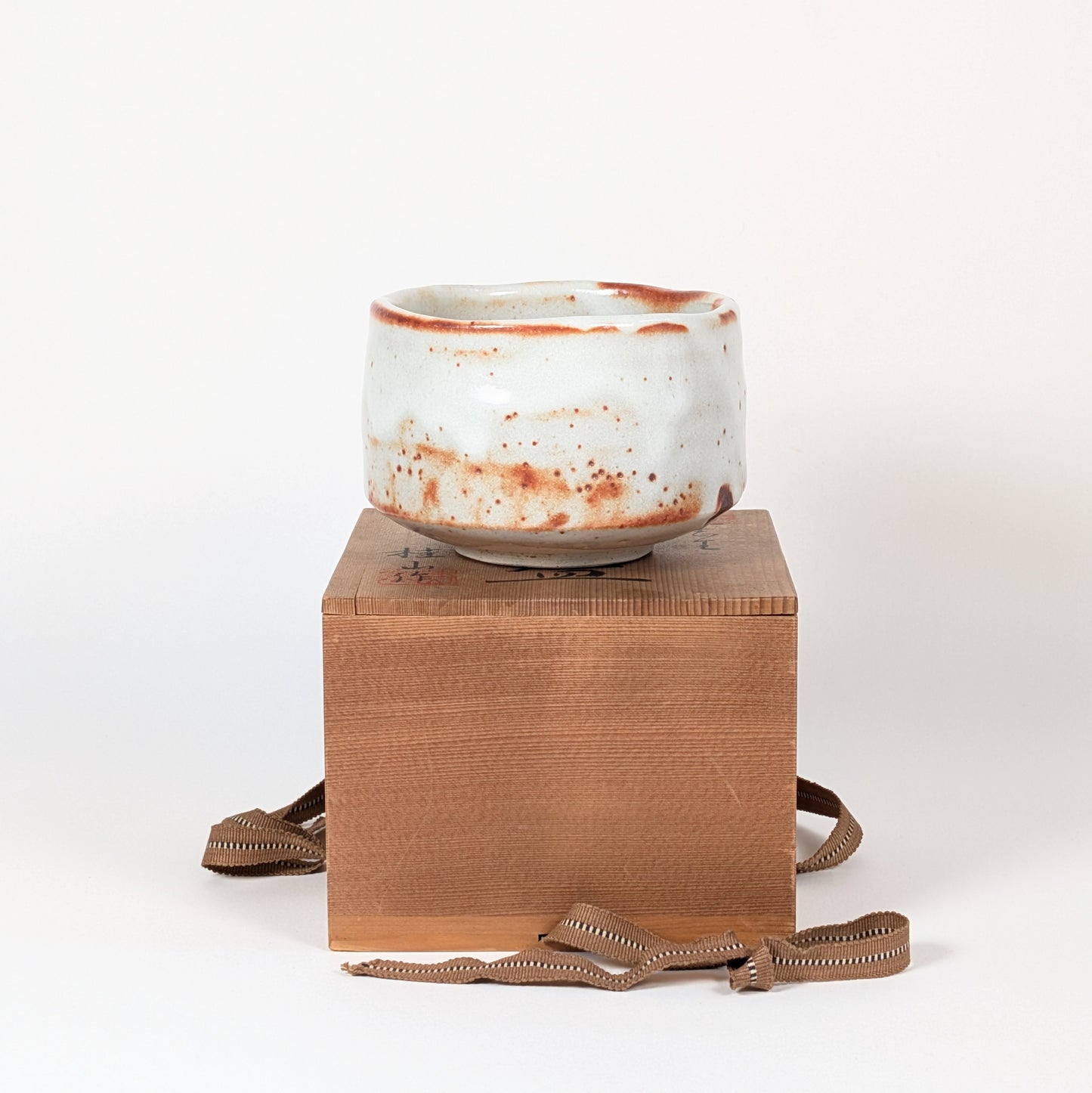 Bol matcha japonais Beni Shino posé sur son tomobako signé, chawan artisanal en céramique Shino pour chanoyu et cérémonie du thé.