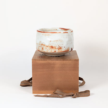 Bol matcha japonais Beni Shino posé sur son tomobako signé, chawan artisanal en céramique Shino pour chanoyu et cérémonie du thé.